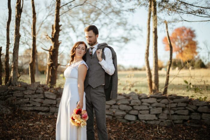bride and groom in front of a small rock wall with trees in the background