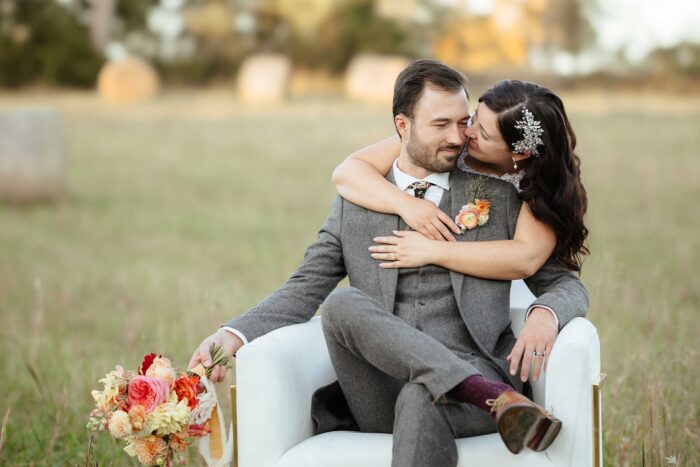 bride hugging her groom from behind while he is sitting down and holding her flowers
